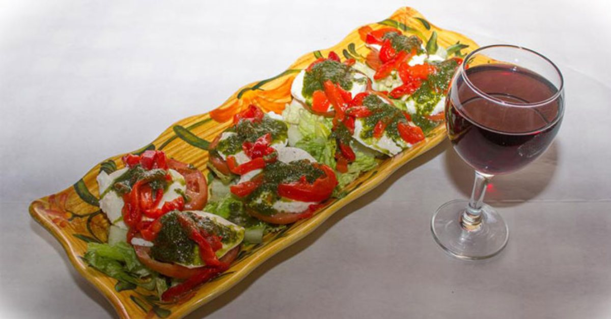 platter of tomatoes with pesto and peppers next to a glass of wine