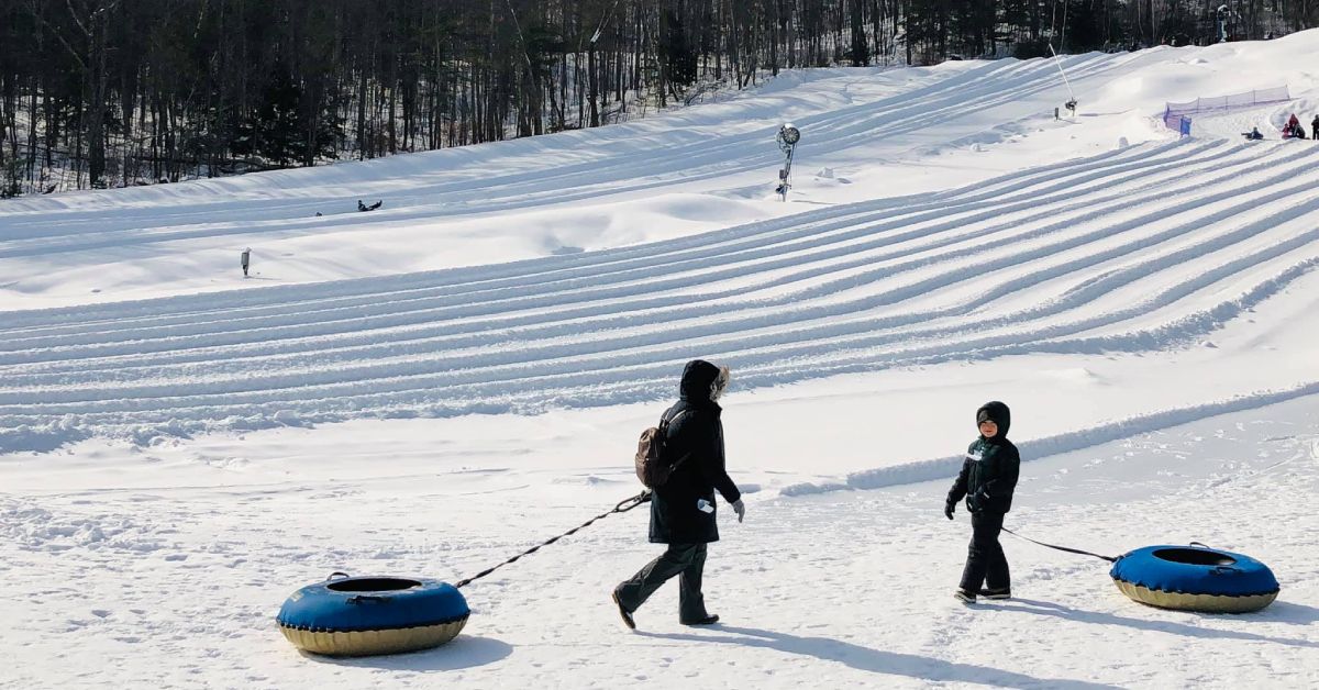 woman and kid with blue snow tubes near a hill
