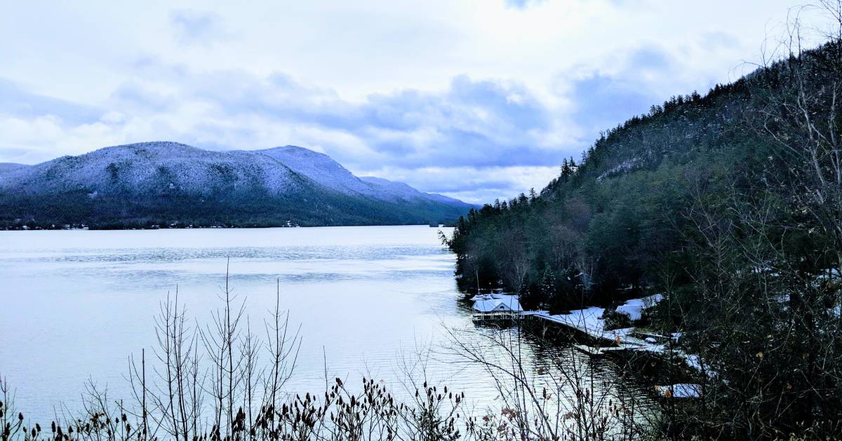 a beautiful view of a lake with mountain and trees in the winter