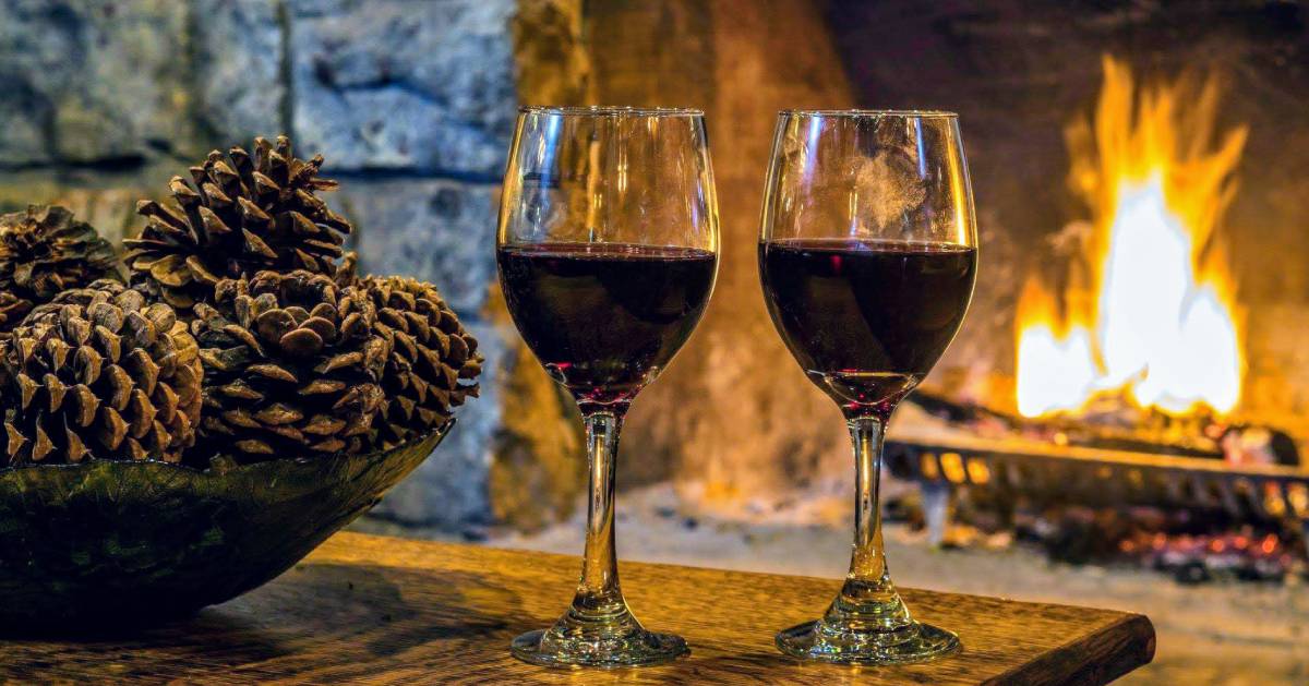 two glasses of red wine in front of a fireplace