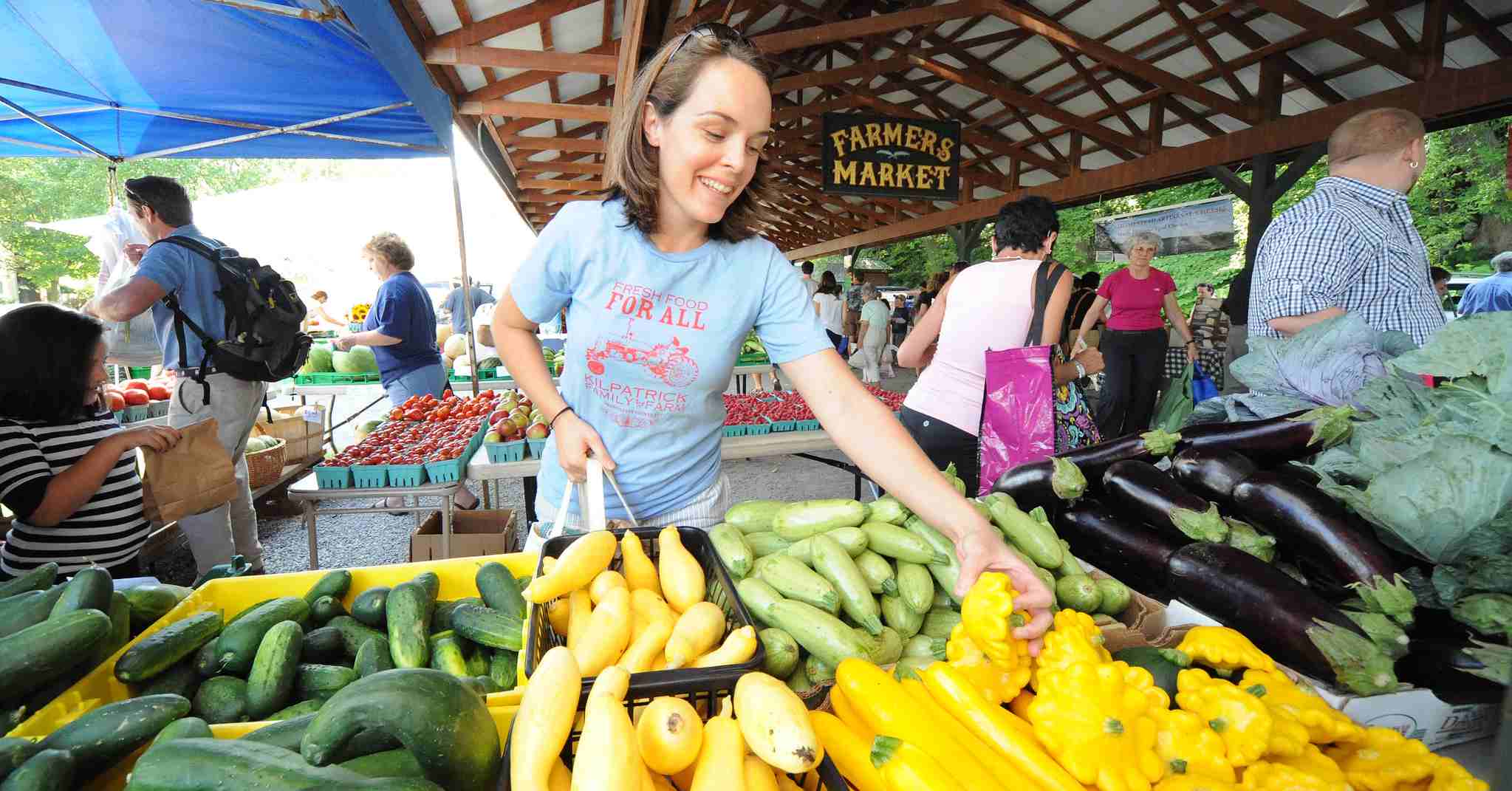 woman reaching for yellow squash at a farmers market