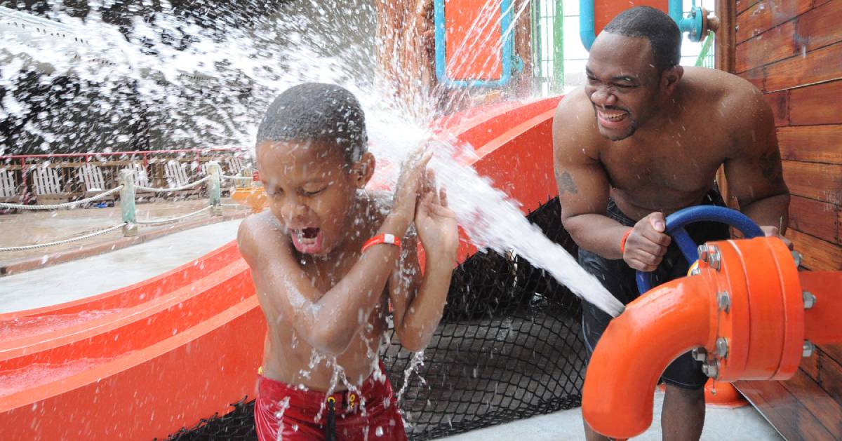 man and his son at indoor waterpark, he's splashing his son with water from a spout