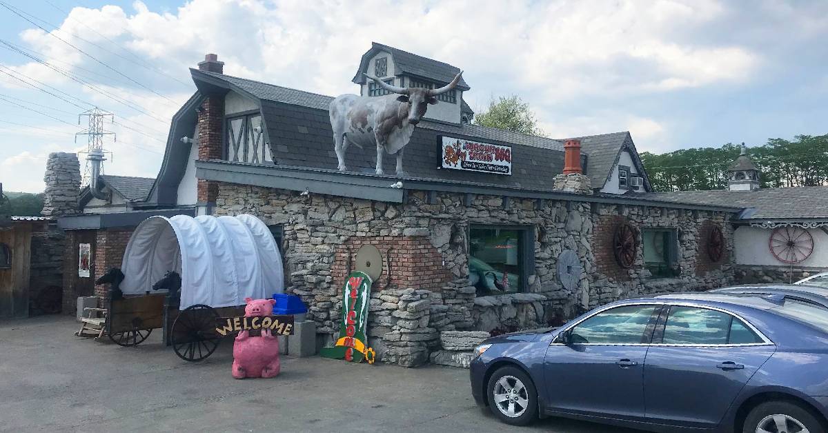 outside a restaurant with steer statue on roof, a covered wagon entrance, and a pig statue with a welcome sign