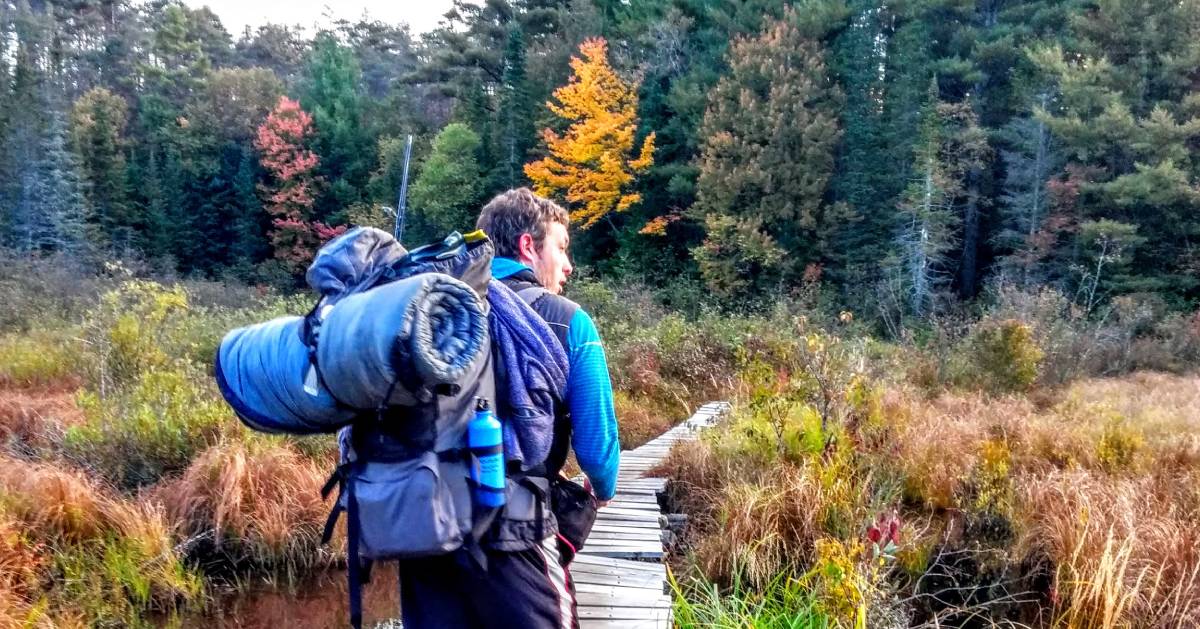 man with camping gear heading into woods in fall