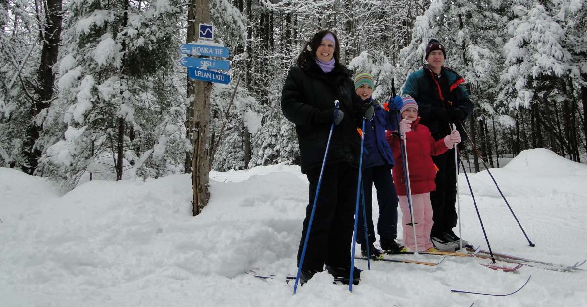two adults and two kids wearing cross country skis on snowy ground