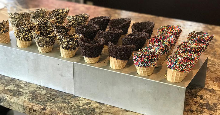 a bunch of ice cream cones, no ice cream, caked with sprinkles, chocolate, or other toppings