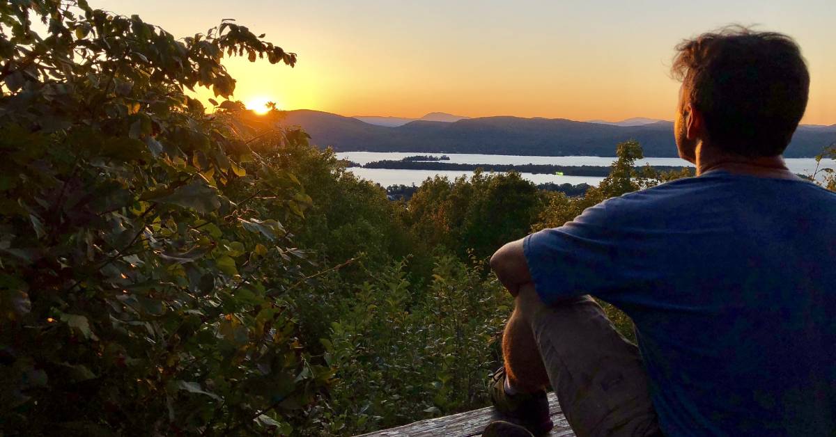 man looks out at sunset from summit
