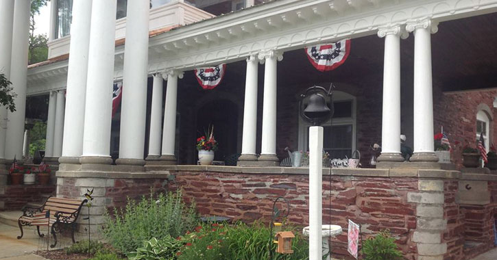 front of mansion with brick wall, bench, and American flags