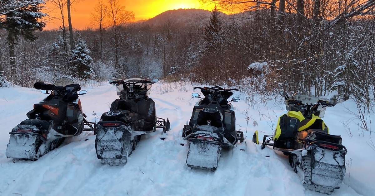 four snowmobiles on a summit at sunset