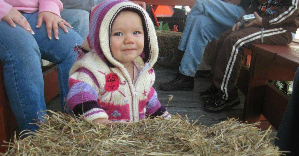 a toddler on a hayride with a pink striped sweater hoodie on