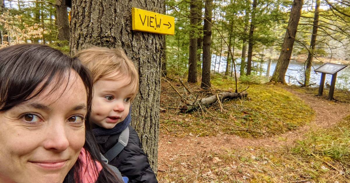 woman hiking with toddler on back takes selfie