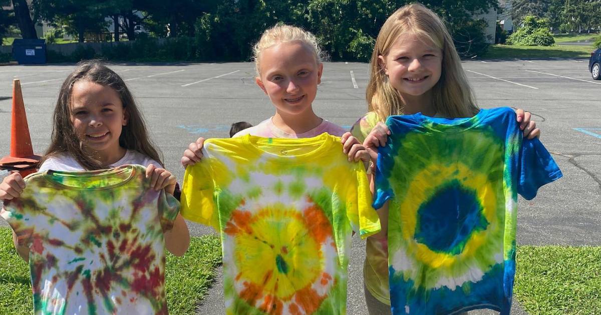 three young girls holding up tye dye shirts