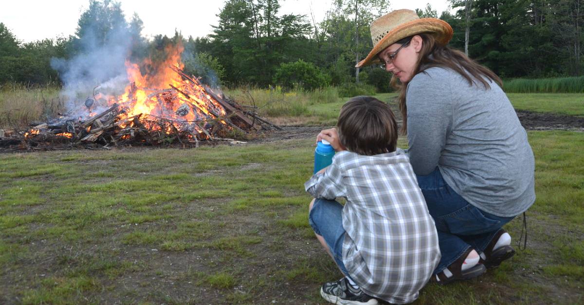 a woman and boy crouching near a bonfire