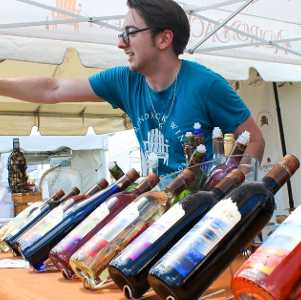 man with glasses pours wine at vendor tent