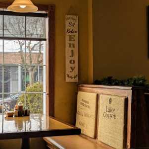 A cozy caf&eacute; interior with a wooden booth, a window overlooking the street, and a wall sign that reads 