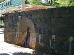 mineral spring jutting out of a stone wall with the saratoga performing arts center entrance visible to the side