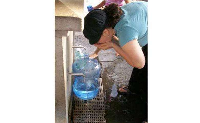 woman filling a large jug with water from a spring