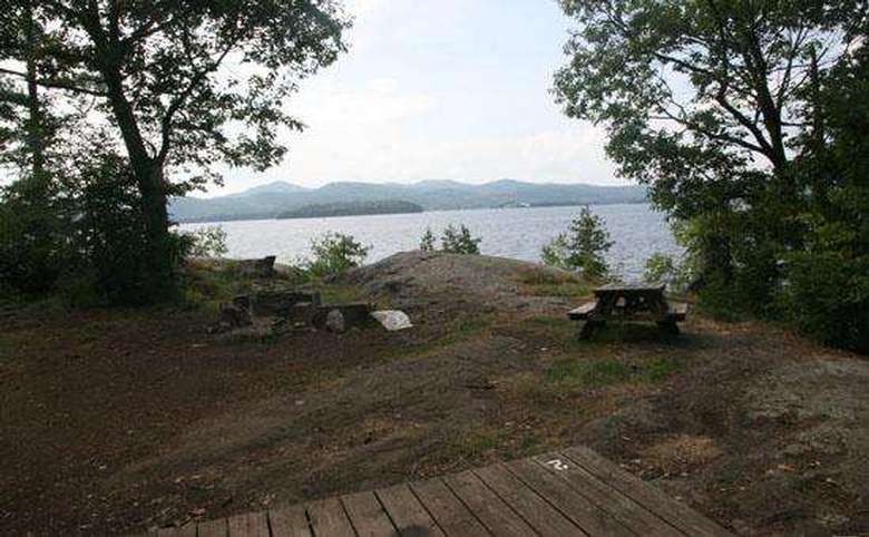 a tent platform, a picnic table, and a fire pit at a campsite with the lake nearby
