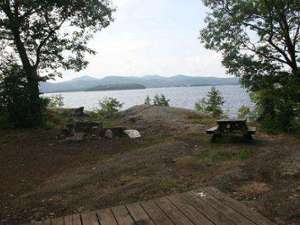 a tent platform, a picnic table, and a fire pit at a campsite with the lake nearby