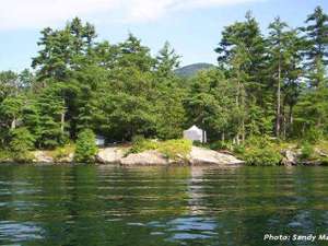 a fairly large island with green trees and a campsite at the shoreline