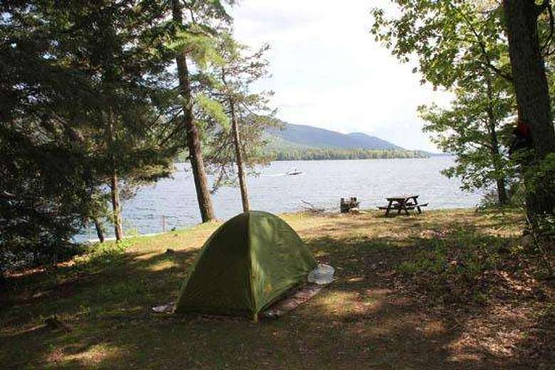 a small green tent set up at a clear and flat campsite near a lake
