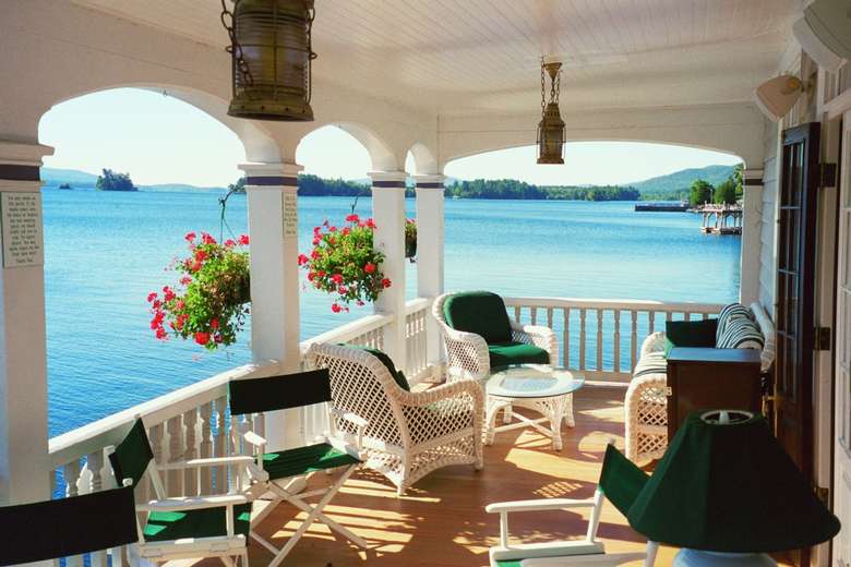 a deck with white and green wicker chairs and a great view of the water
