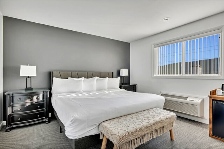a modern hotel room with large bed, dresser, and window