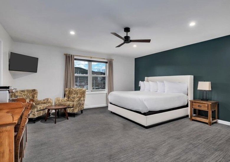 a hotel suite with large bed, two chairs, TV, and other amenities