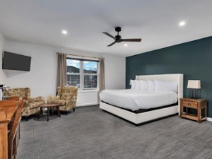 a hotel suite with large bed, two chairs, TV, and other amenities