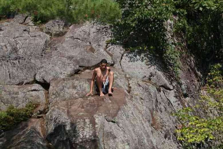 Boy sitting on a cliff preparing to jump into the lake