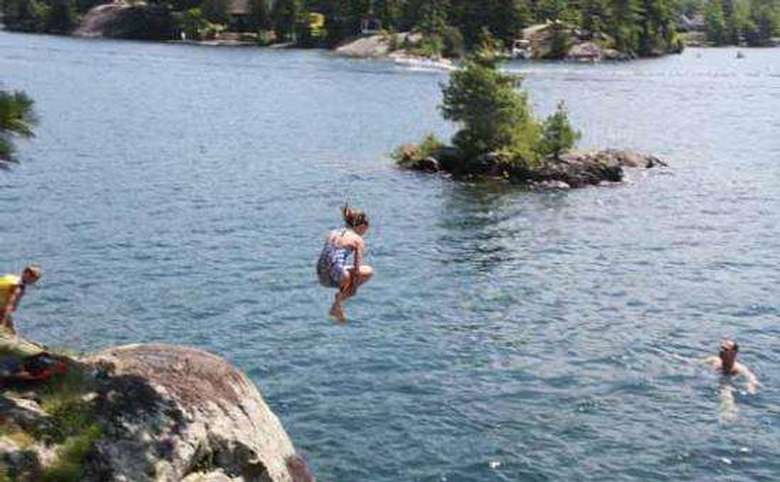 a girl jumping into the water from a cliff, and an island is in the background