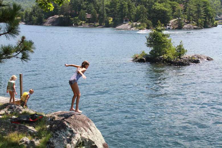a girl preparing to jump from a cliff into a lake with an island in the background