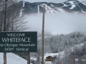 sign that says welcome whiteface the olympic mountain with a ski mountain visible in the background