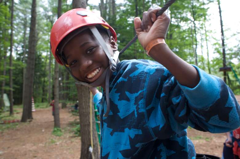 A young boy in a red helmet smiling on a ropes course