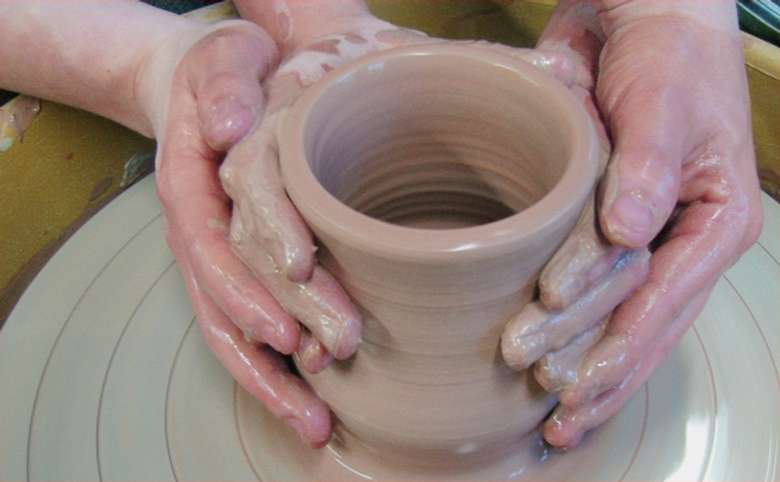 two sets of hands working with clay on a wheel