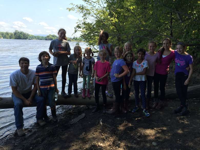 large group of kids standing on a log in front of a lake