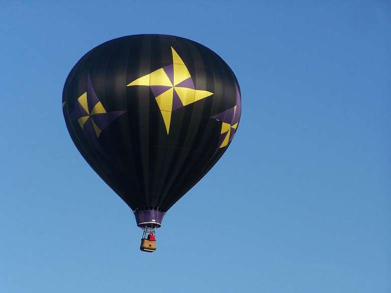 black hot air balloon with yellow pinwheels in flight