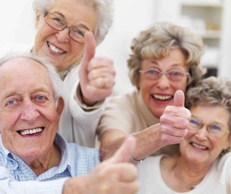 four elderly people smiling and giving thumbs up