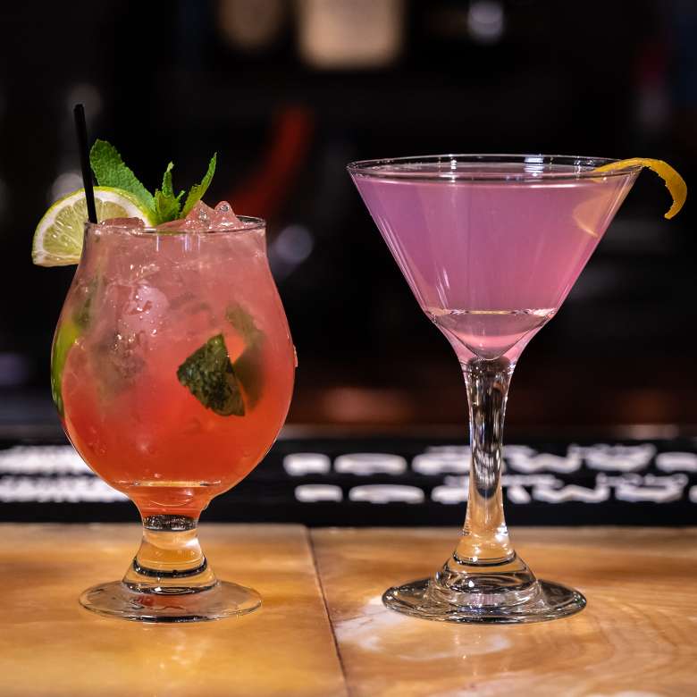 Two pink cocktails on a bar top