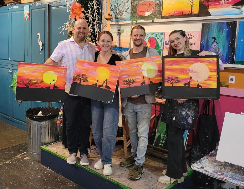 four people holding up their artworks in a studio