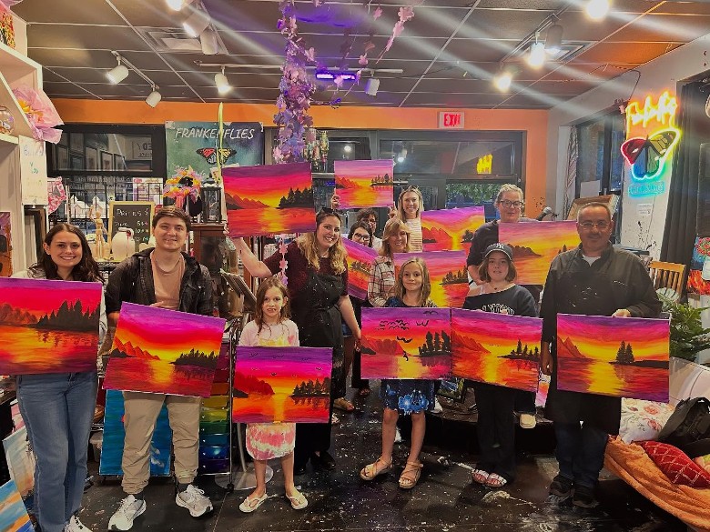 large group of people holding up their artworks in a studio