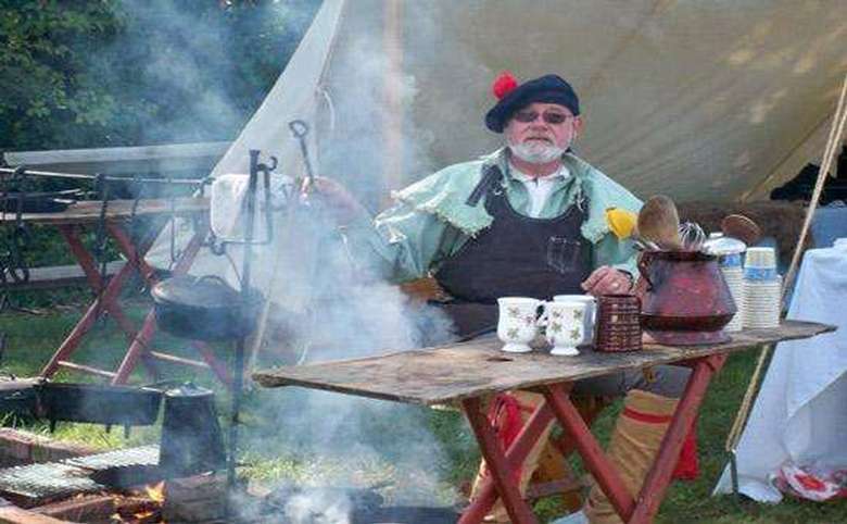 A costumed reenactor cooking over a fire