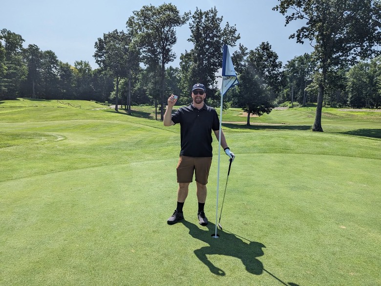 a man standing by a golf hole flag and holding up a ball