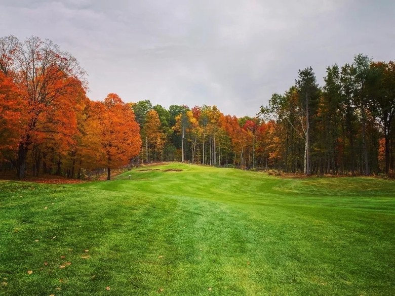 a golf course with orange colors on the trees during the fall season