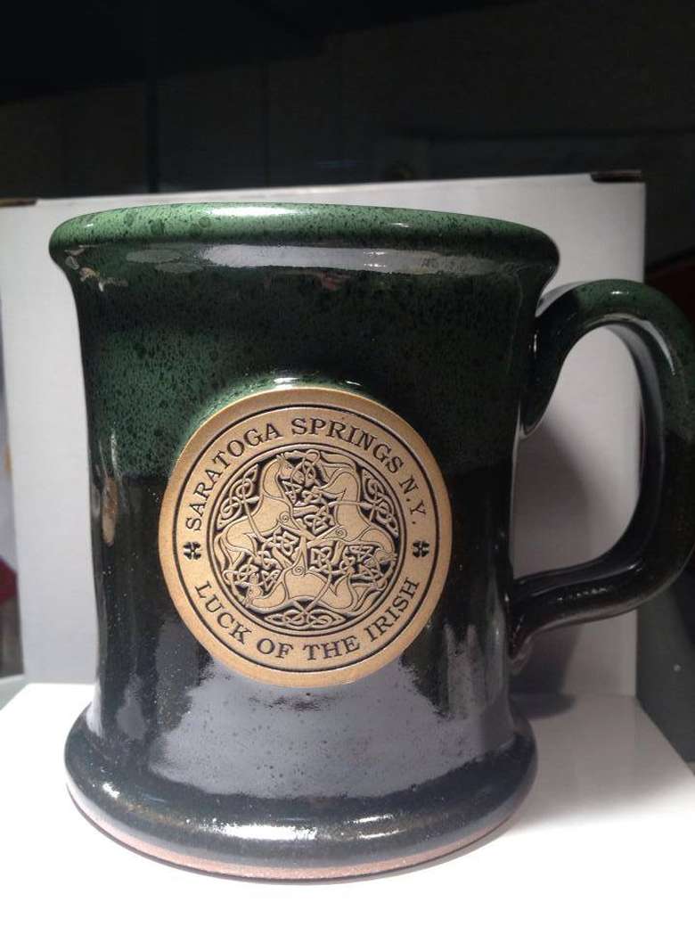 dark green coffee mug with a gold circle that says saratoga springs ny luck of the irish