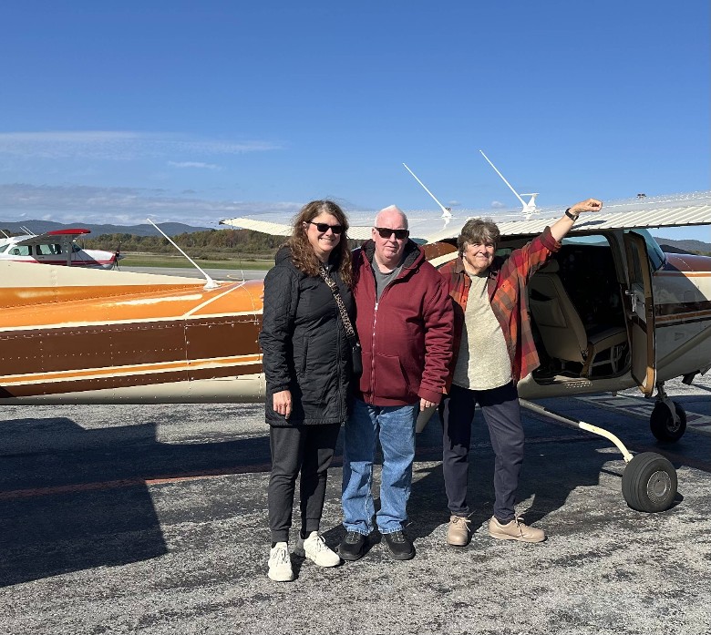 three people pose by small plane