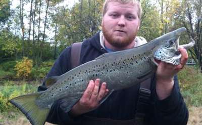 man with beard holding up fish caught in saranac river