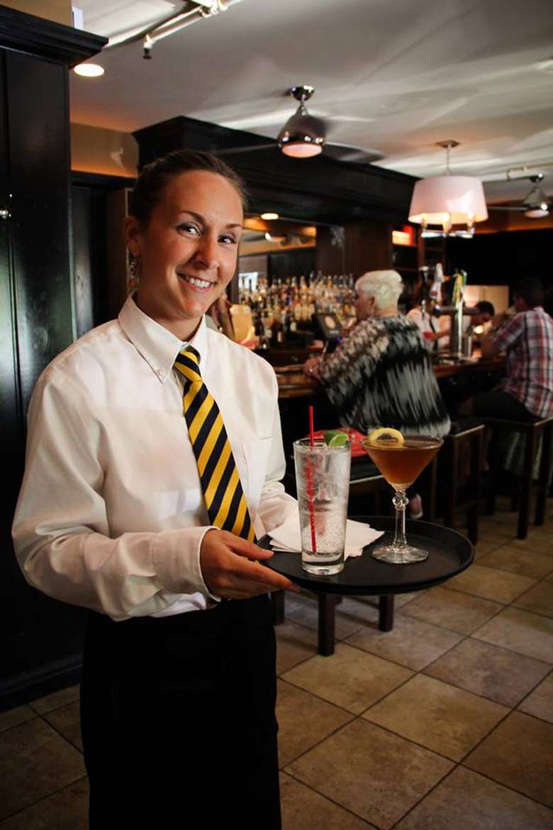 waitress wearing a striped tie holding a tray with two drinks on it