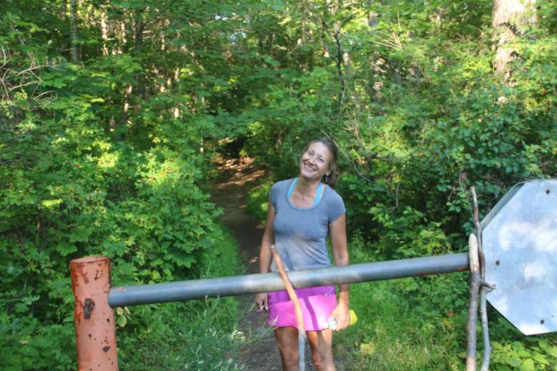 woman standing next to a barrier keeping cars off of a hiking trail