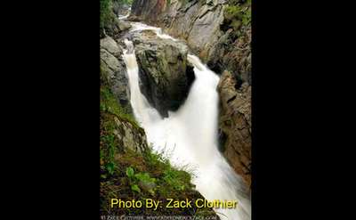 waterfall being split by a large rock and then coming back together with photo credit by zack clothier